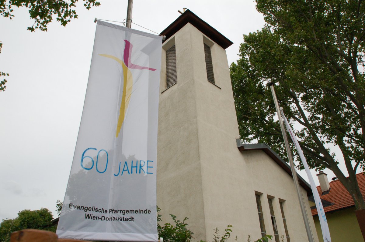 Seit 60 Jahren steht die Bekenntniskirche an der Erzherzog-Karl-Straße in Donaustadt. (c) M. Schomaker Fahner mit dem Kirchenlogo und einem aufgemalten Schriftzug "60 Jahre"