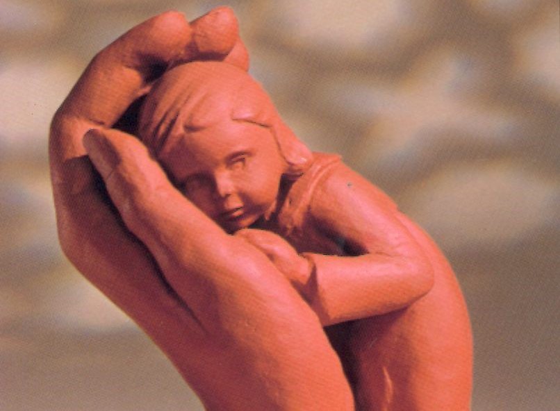 Geborgen in Gottes Hand. (c) Dorothea Steigerwald Ton-Figur: eine Hand hält tröstend ein Kind.